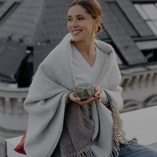Smiling woman wrapped in a blanket holding a teacup on a rooftop - Walmsley Dental brand design